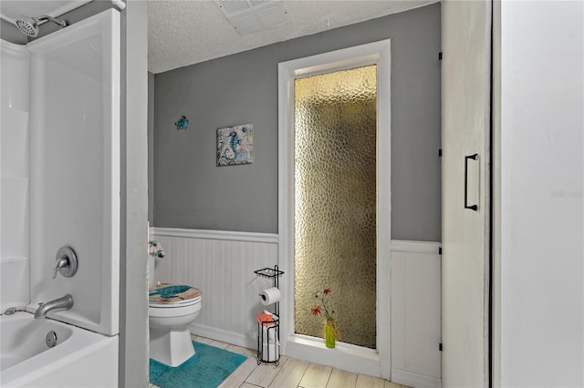 bathroom with a textured ceiling, hardwood / wood-style flooring, shower / washtub combination, and toilet