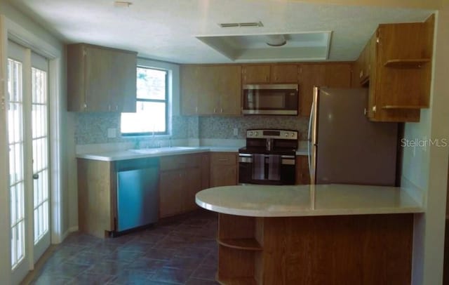 kitchen featuring sink, kitchen peninsula, appliances with stainless steel finishes, and decorative backsplash