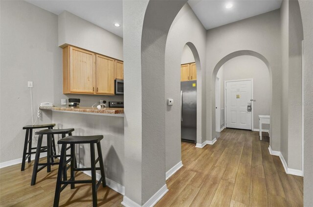 kitchen featuring a kitchen breakfast bar, light hardwood / wood-style floors, kitchen peninsula, light brown cabinets, and stainless steel appliances