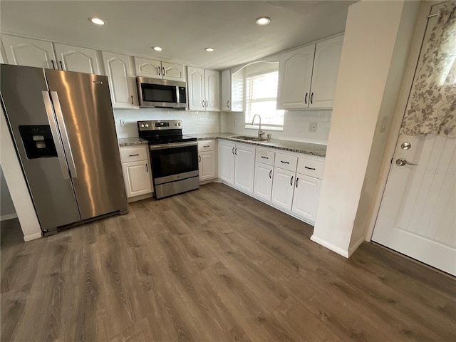 kitchen featuring appliances with stainless steel finishes, white cabinetry, light stone counters, dark hardwood / wood-style flooring, and sink