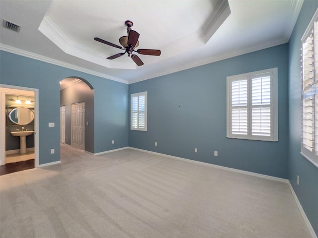 unfurnished bedroom with ensuite bath, light colored carpet, ornamental molding, and multiple windows