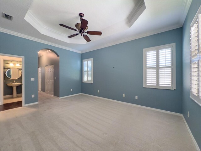 4977 Sapphire Sound Dr, Wimauma, FL 33598 - unfurnished bedroom with carpet floors, crown molding, arched walkways, a tray ceiling, and a ceiling fan