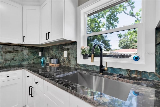 kitchen with decorative backsplash, dark stone countertops, white cabinetry, and sink