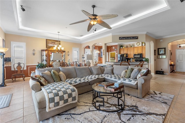 tiled living room featuring plenty of natural light, crown molding, ceiling fan with notable chandelier, and a tray ceiling