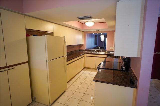 kitchen with white refrigerator, sink, black range, a raised ceiling, and light tile patterned floors