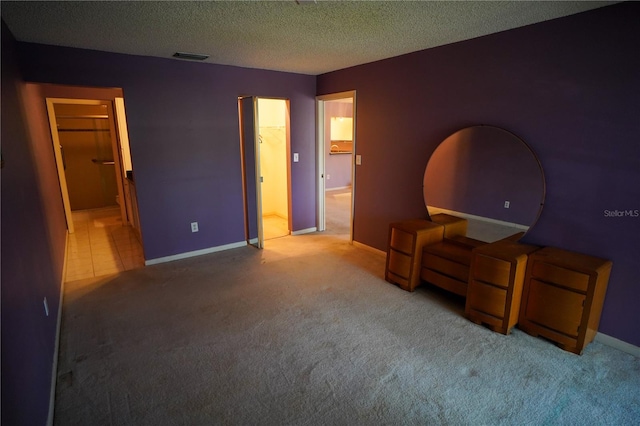 bedroom with a spacious closet, a closet, a textured ceiling, carpet flooring, and ensuite bath