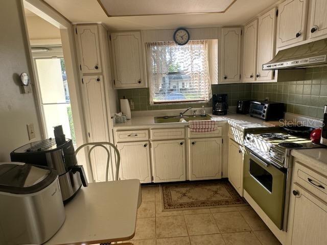 kitchen featuring backsplash, stainless steel range, light tile patterned floors, and sink