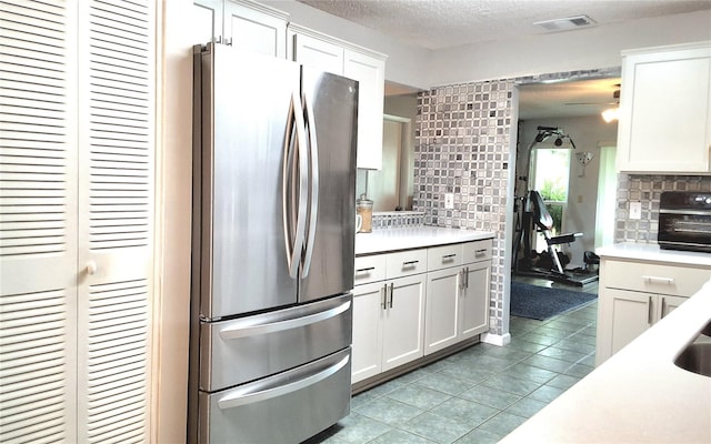 kitchen featuring stainless steel fridge, white cabinetry, tasteful backsplash, light tile patterned floors, and a textured ceiling