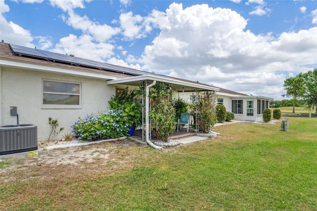 rear view of property featuring a yard, solar panels, and central air condition unit