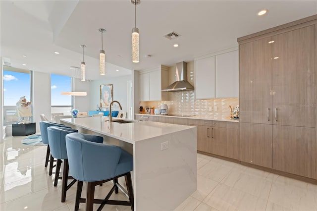 kitchen featuring sink, wall chimney exhaust hood, backsplash, decorative light fixtures, and a spacious island