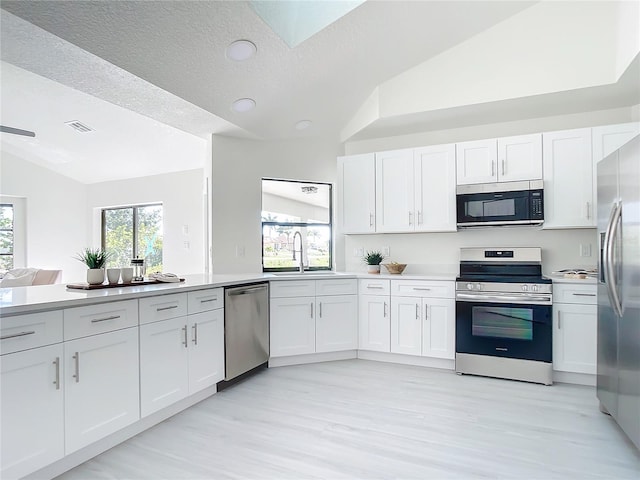 kitchen with appliances with stainless steel finishes, a textured ceiling, light hardwood / wood-style floors, lofted ceiling, and white cabinets