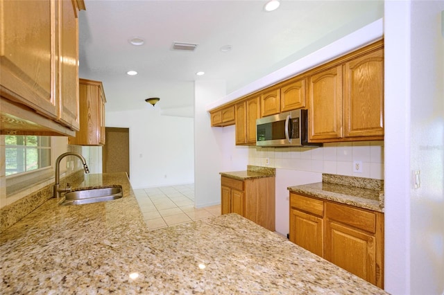 kitchen with decorative backsplash, light stone counters, light tile patterned floors, and sink