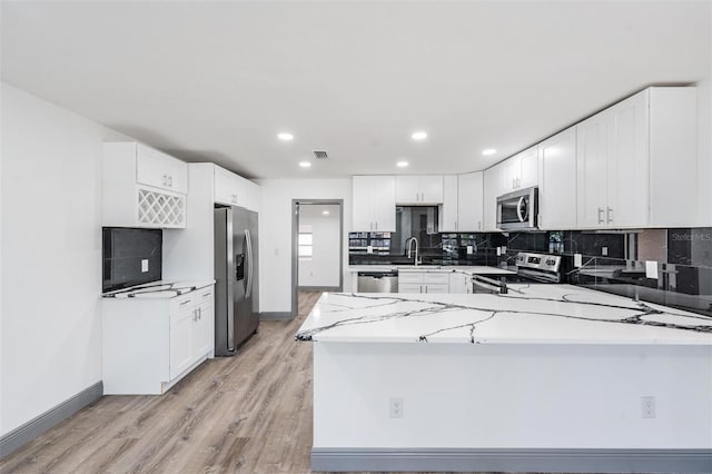 kitchen with stainless steel appliances, white cabinetry, light stone counters, and light wood-type flooring