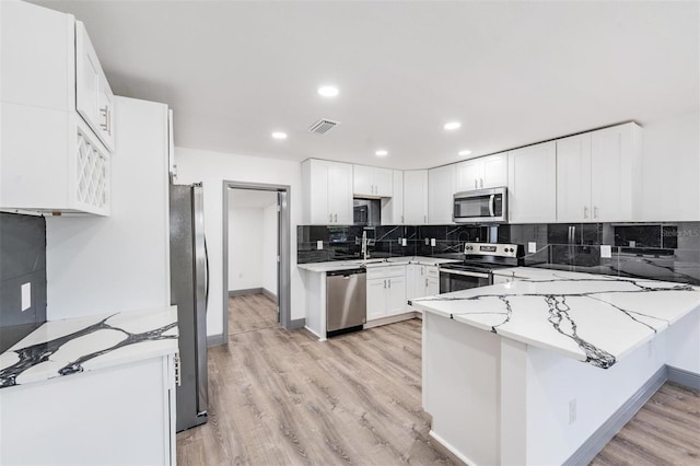 kitchen with light stone counters, white cabinets, kitchen peninsula, light hardwood / wood-style flooring, and stainless steel appliances