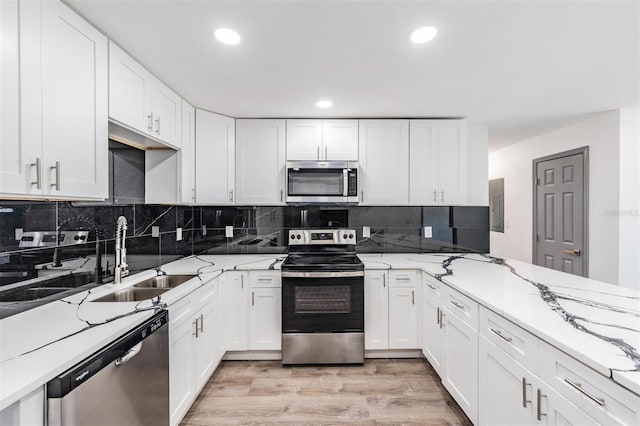 kitchen featuring sink, light hardwood / wood-style flooring, white cabinetry, stainless steel appliances, and light stone countertops