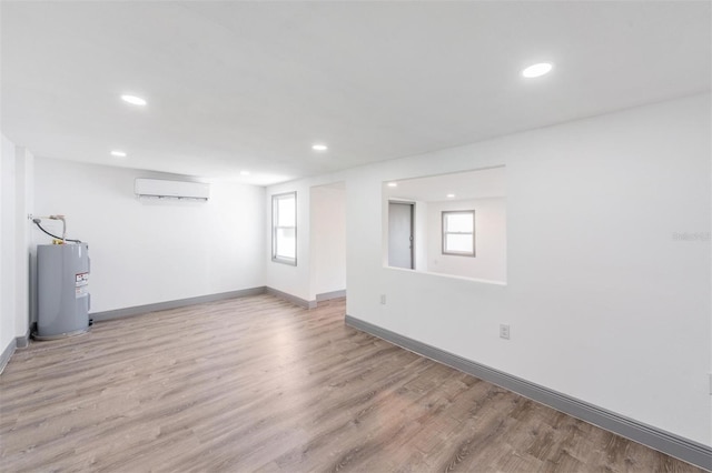 spare room with electric water heater, light wood-type flooring, plenty of natural light, and a wall mounted air conditioner