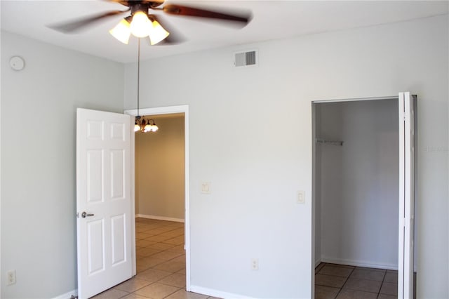 unfurnished bedroom with a closet, tile patterned flooring, a spacious closet, and ceiling fan with notable chandelier