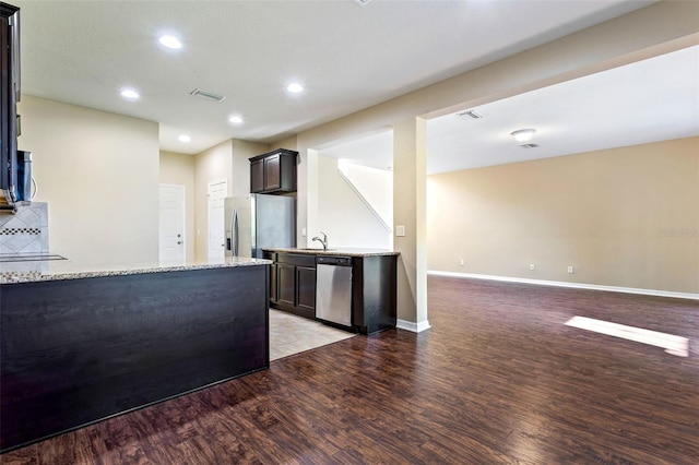 kitchen with light hardwood / wood-style floors, light stone counters, tasteful backsplash, stainless steel appliances, and dark brown cabinetry