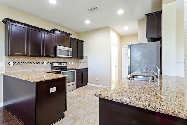 kitchen with dark brown cabinetry, sink, kitchen peninsula, stainless steel appliances, and light stone countertops