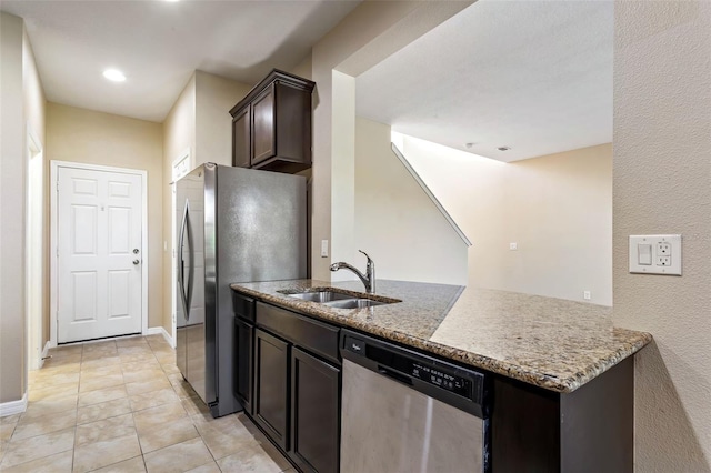 kitchen with kitchen peninsula, light stone countertops, stainless steel appliances, dark brown cabinets, and sink