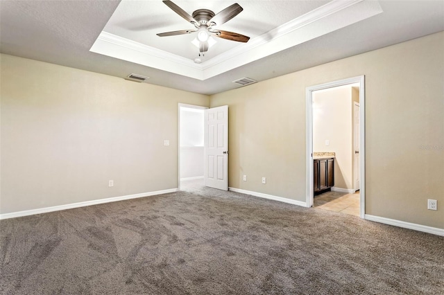 unfurnished bedroom featuring a tray ceiling, light carpet, ensuite bath, crown molding, and ceiling fan