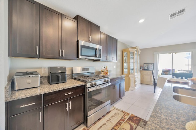 kitchen with dark brown cabinets, stainless steel appliances, stone counters, and light tile patterned floors