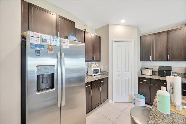 kitchen featuring dark brown cabinetry, light tile patterned flooring, stainless steel fridge with ice dispenser, and light stone counters