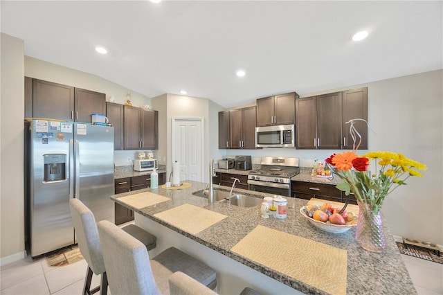 kitchen featuring a breakfast bar, vaulted ceiling, appliances with stainless steel finishes, light tile patterned floors, and dark brown cabinetry