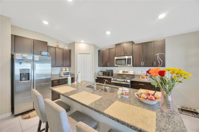 kitchen featuring light tile patterned flooring, a breakfast bar area, stainless steel appliances, lofted ceiling, and dark brown cabinetry