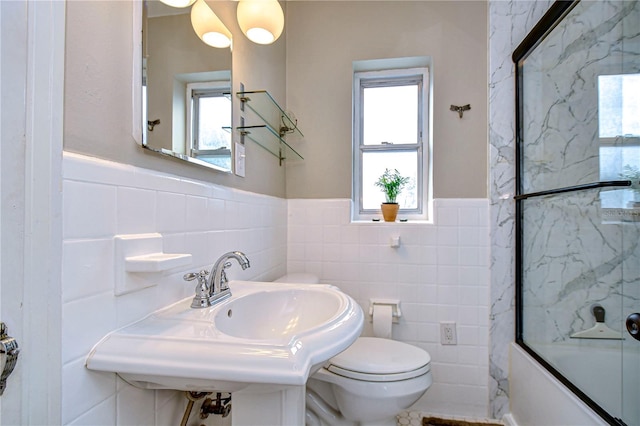 full bathroom with tile walls, bath / shower combo with glass door, toilet, and a wealth of natural light