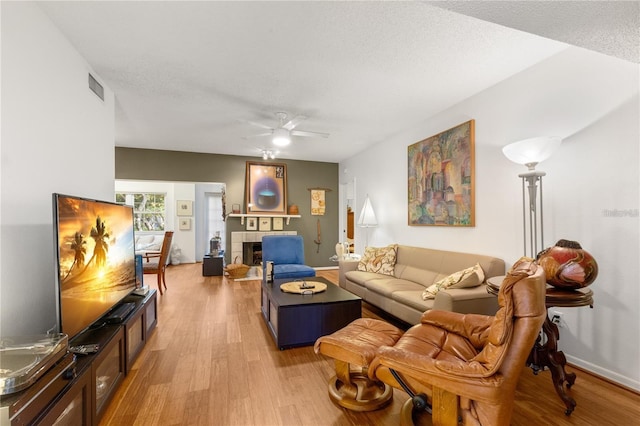 living room featuring a tile fireplace, ceiling fan, a textured ceiling, and light hardwood / wood-style floors