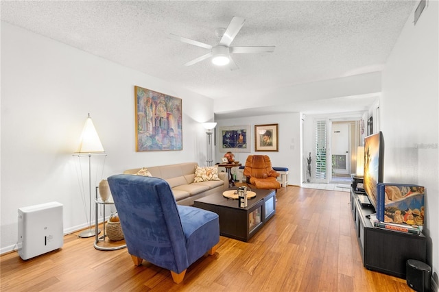 living room with ceiling fan, a textured ceiling, and light wood-type flooring