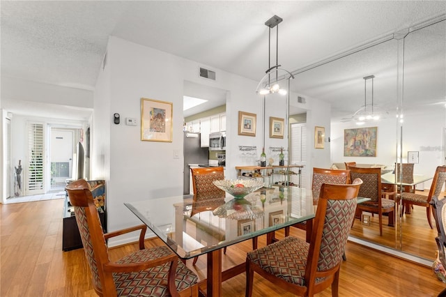 dining room with a notable chandelier, a textured ceiling, and light wood-type flooring