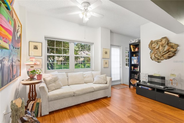 living room featuring ceiling fan, light hardwood / wood-style flooring, and a textured ceiling