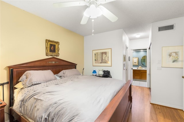 bedroom with ceiling fan, connected bathroom, a textured ceiling, and light hardwood / wood-style floors