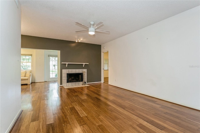 unfurnished living room featuring a tiled fireplace, wood-type flooring, ceiling fan, and a textured ceiling