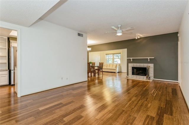 living room with a tiled fireplace, hardwood / wood-style flooring, ceiling fan with notable chandelier, and a textured ceiling