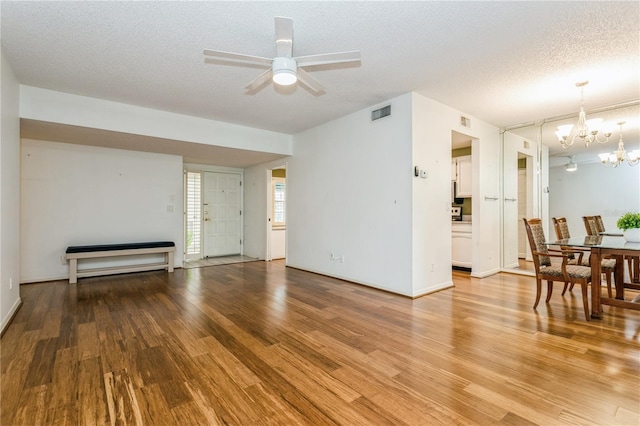 living room featuring ceiling fan with notable chandelier, light hardwood / wood-style floors, and a textured ceiling