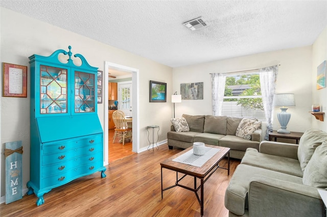 living room featuring baseboards, a textured ceiling, visible vents, and wood finished floors