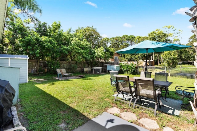 view of yard with an outbuilding, a fenced backyard, a patio, a storage unit, and outdoor dining space