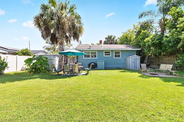 rear view of property featuring an outbuilding, a fenced backyard, a storage unit, an outdoor fire pit, and a yard