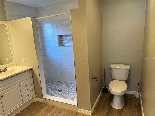 bathroom with wood-type flooring, a tile shower, vanity, and toilet