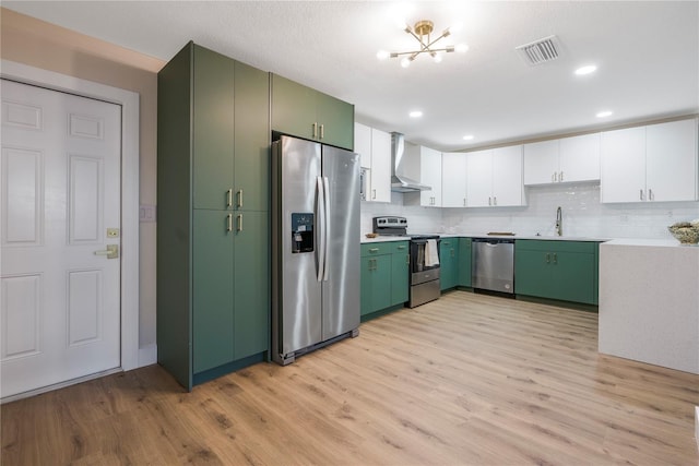 kitchen featuring stainless steel appliances, light wood-type flooring, wall chimney range hood, green cabinetry, and white cabinets