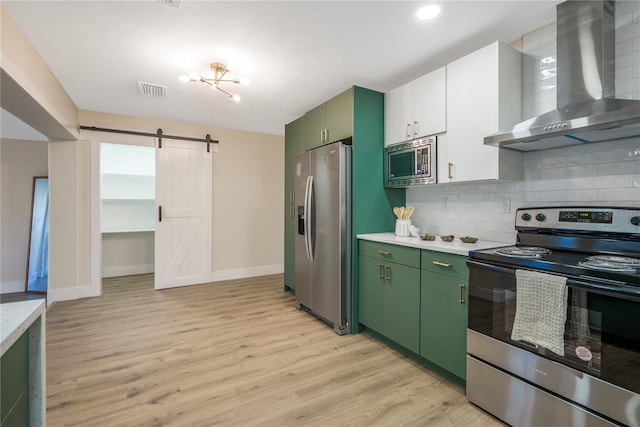 kitchen with wall chimney range hood, appliances with stainless steel finishes, a barn door, and light hardwood / wood-style floors