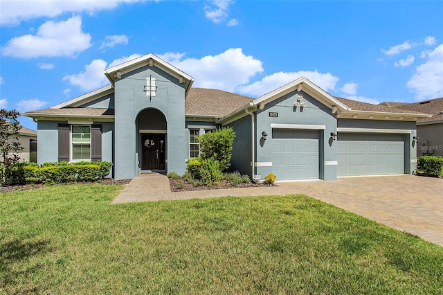 view of front facade with an attached garage, decorative driveway, a front yard, and stucco siding