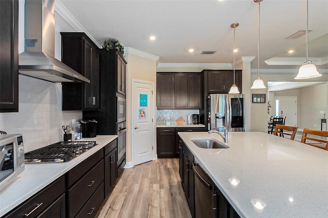 kitchen with wall chimney exhaust hood, light stone counters, stainless steel appliances, pendant lighting, and a sink