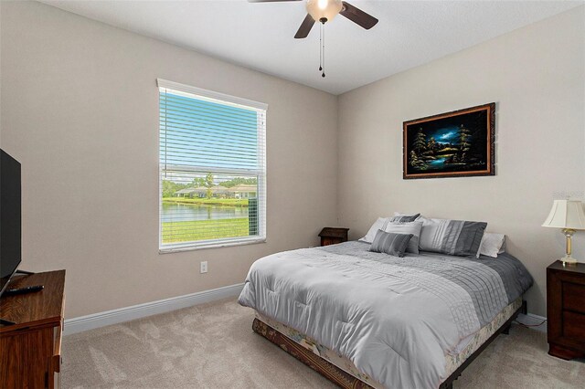 bedroom with light carpet, ceiling fan, a water view, and baseboards