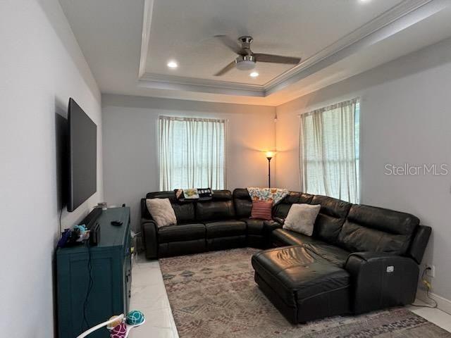 living room featuring crown molding, ceiling fan, plenty of natural light, and a tray ceiling