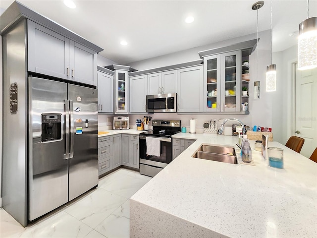 kitchen featuring sink, light stone counters, appliances with stainless steel finishes, gray cabinets, and pendant lighting