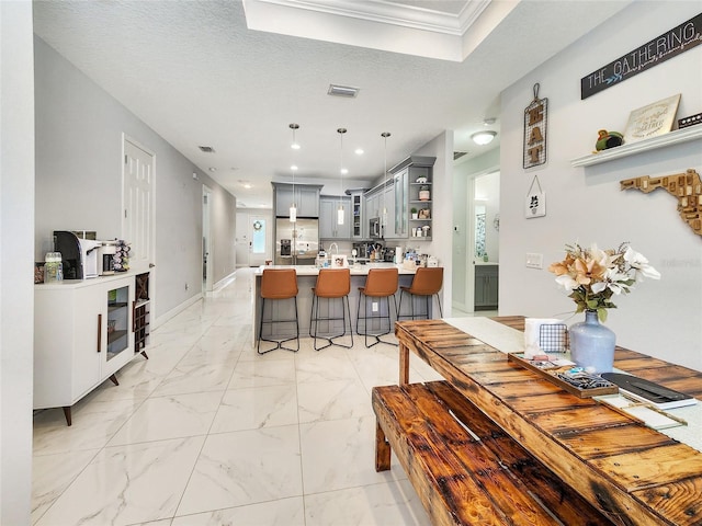 kitchen featuring gray cabinetry, decorative light fixtures, ornamental molding, appliances with stainless steel finishes, and a kitchen breakfast bar